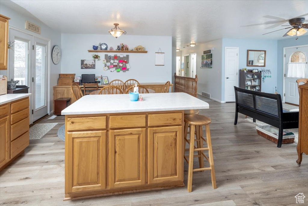 Kitchen with a kitchen breakfast bar, light wood-type flooring, ceiling fan, and a center island