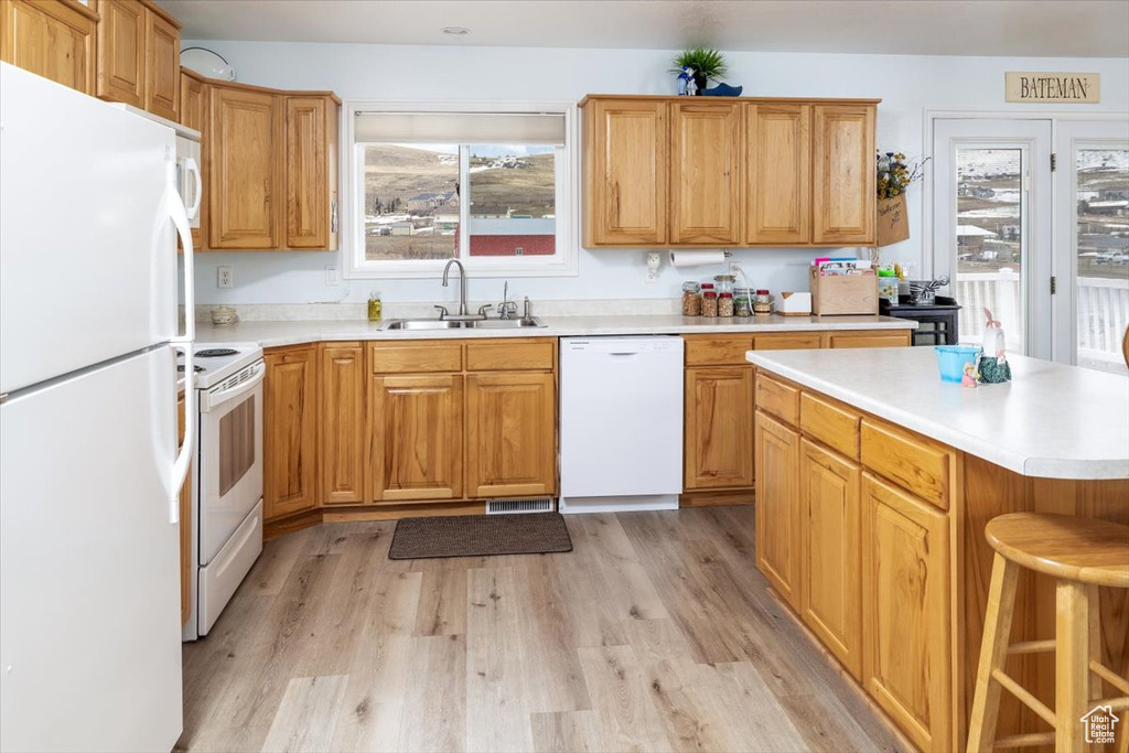 Kitchen featuring light hardwood / wood-style flooring, white appliances, a center island, and sink