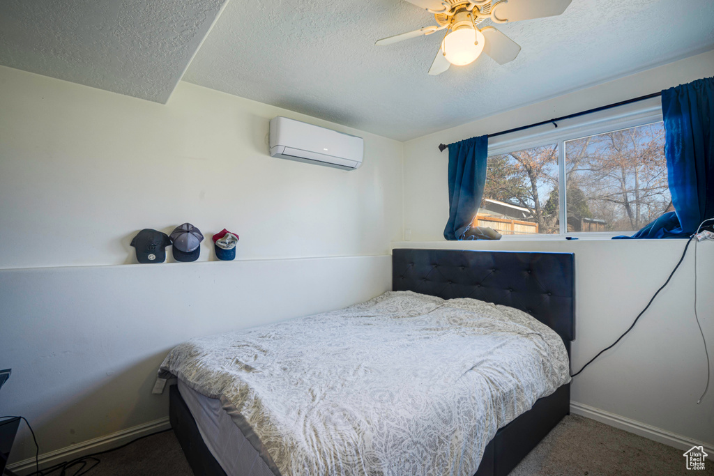 Bedroom with a wall mounted AC, a textured ceiling, dark carpet, and ceiling fan