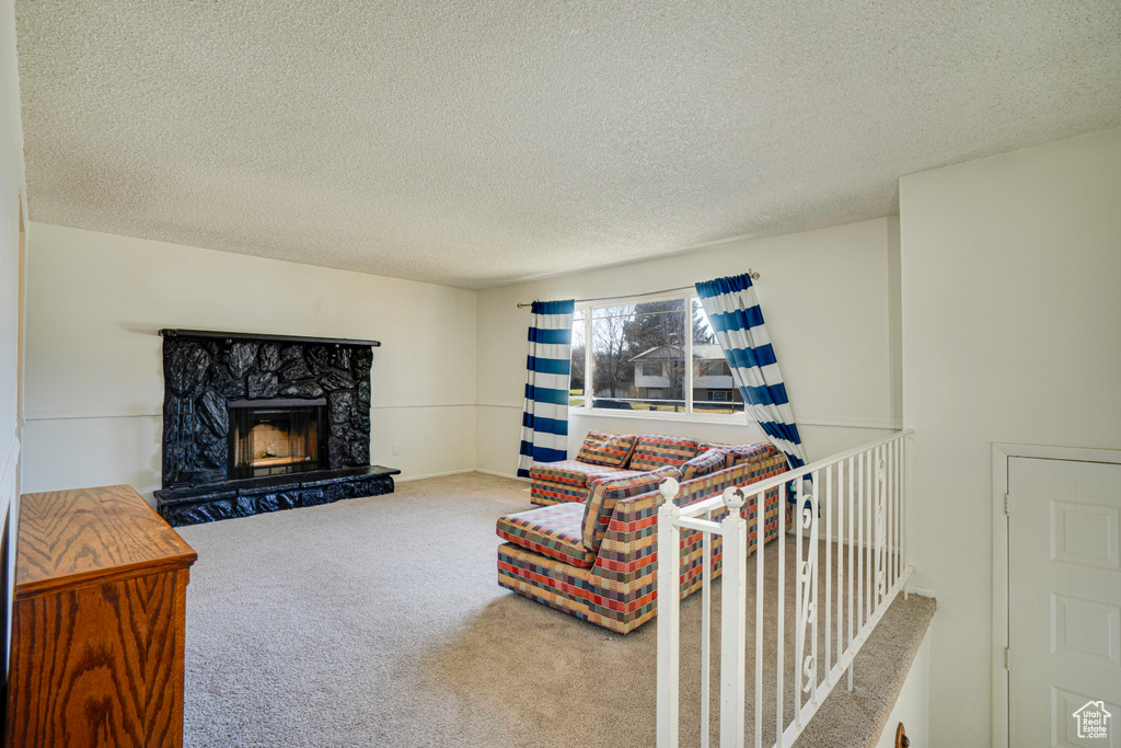 Living room featuring a stone fireplace, carpet, and a textured ceiling