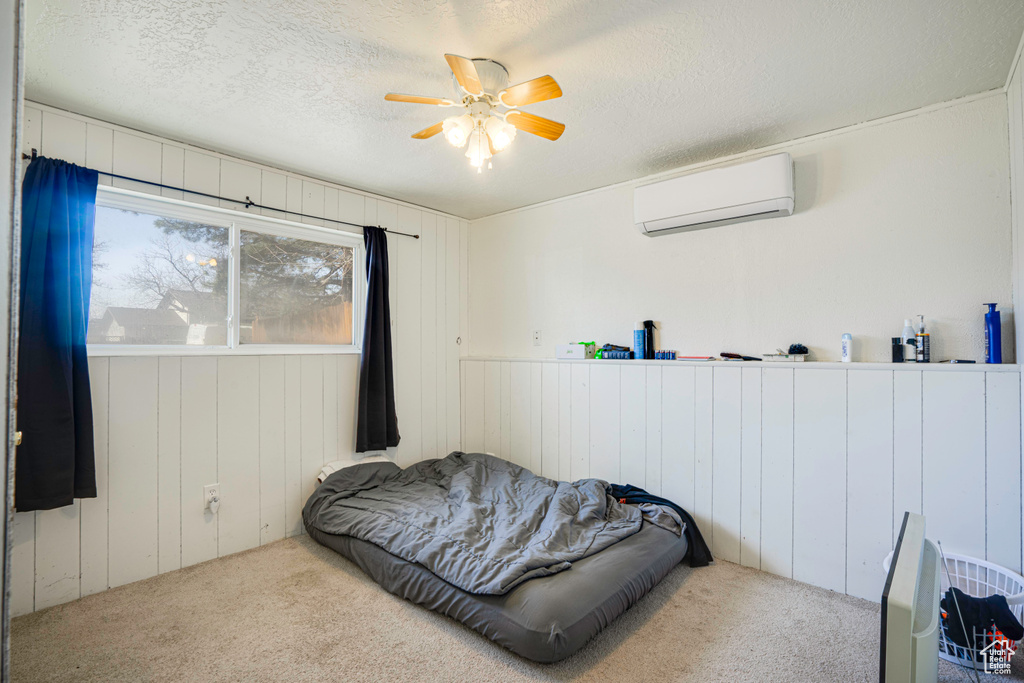 Carpeted bedroom featuring a textured ceiling, a wall mounted air conditioner, and ceiling fan
