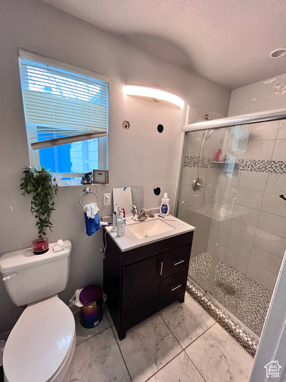 Bathroom featuring vanity with extensive cabinet space, a textured ceiling, a shower with door, toilet, and tile floors