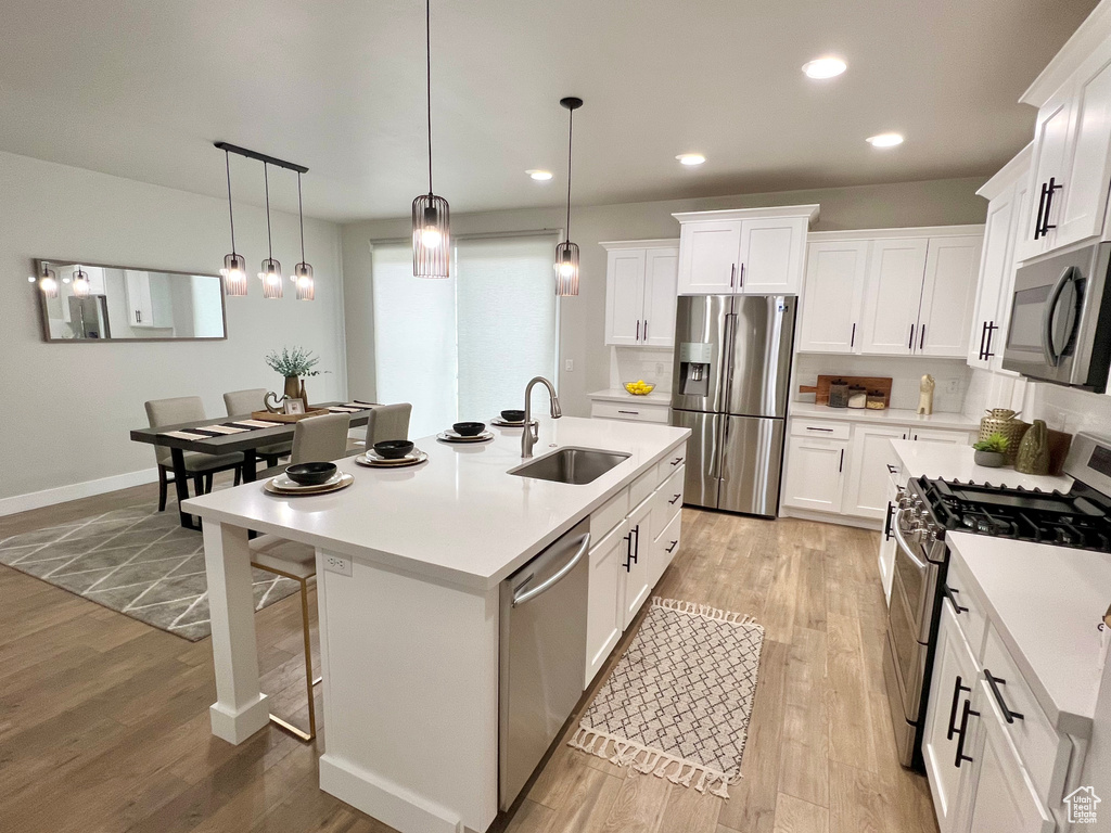 Kitchen featuring appliances with stainless steel finishes, pendant lighting, light hardwood / wood-style floors, and sink