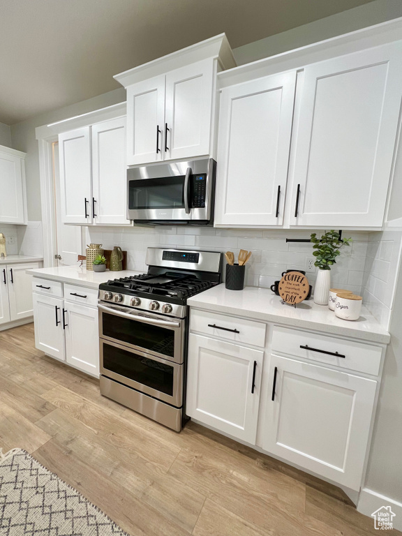 Kitchen featuring backsplash, stainless steel appliances, light wood-type flooring, and white cabinetry