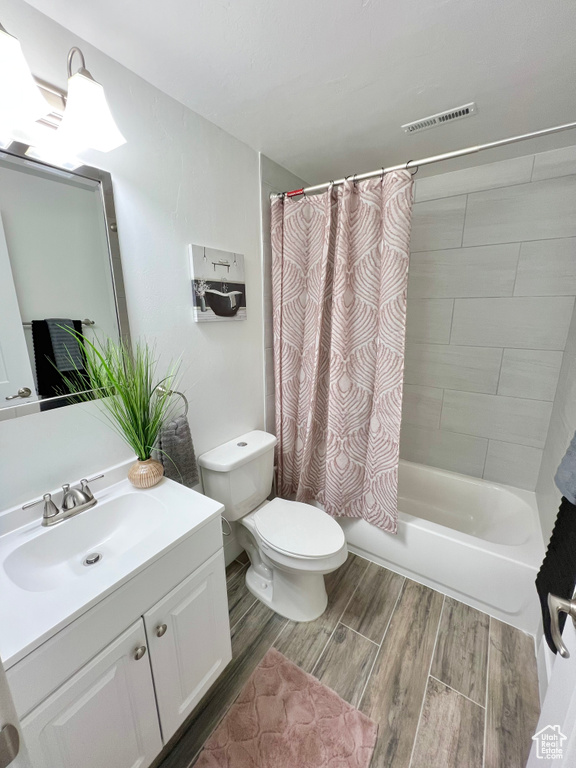Full bathroom featuring vanity with extensive cabinet space, hardwood / wood-style flooring, shower / tub combo, and toilet