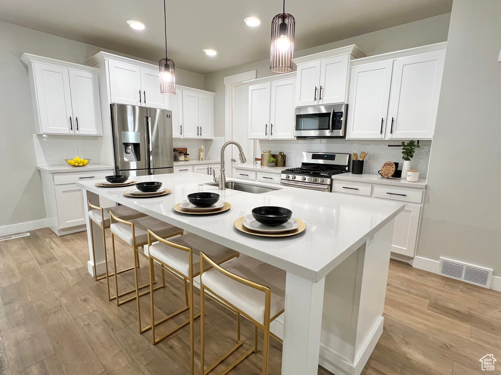 Kitchen with appliances with stainless steel finishes, a kitchen breakfast bar, hanging light fixtures, and light hardwood / wood-style floors