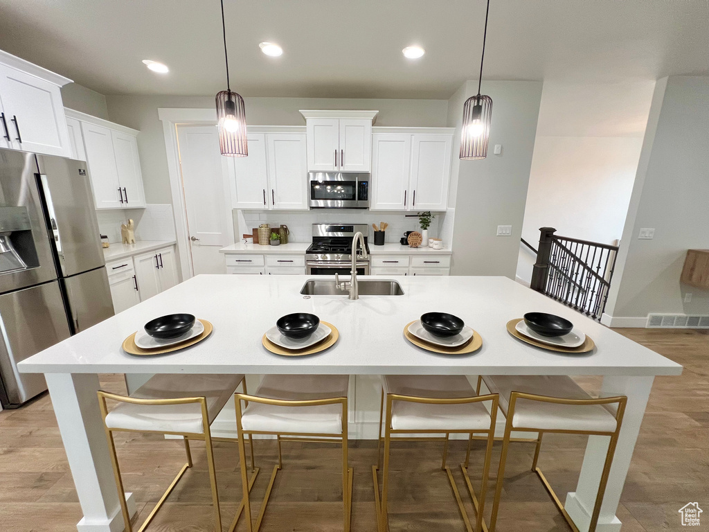 Kitchen featuring appliances with stainless steel finishes, pendant lighting, light wood-type flooring, and sink