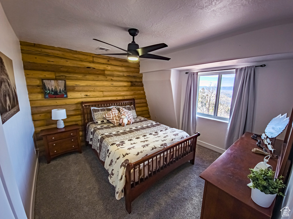 Bedroom featuring dark colored carpet, rustic walls, a textured ceiling, and ceiling fan