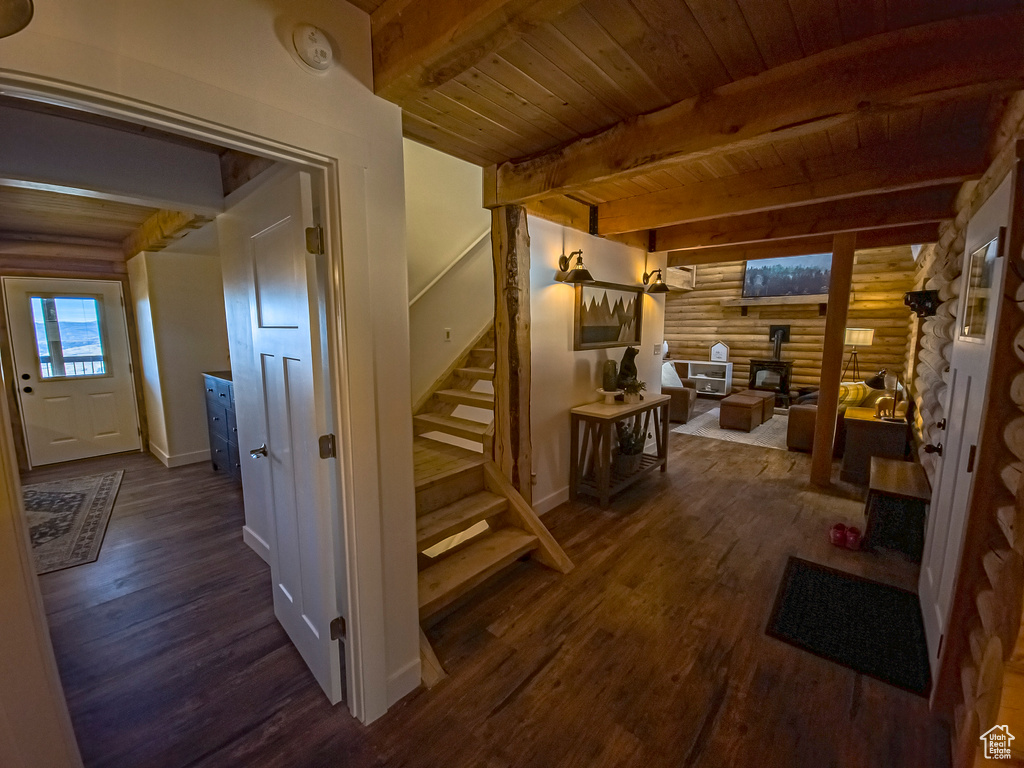Stairway with dark hardwood / wood-style floors, rustic walls, wooden ceiling, and beamed ceiling