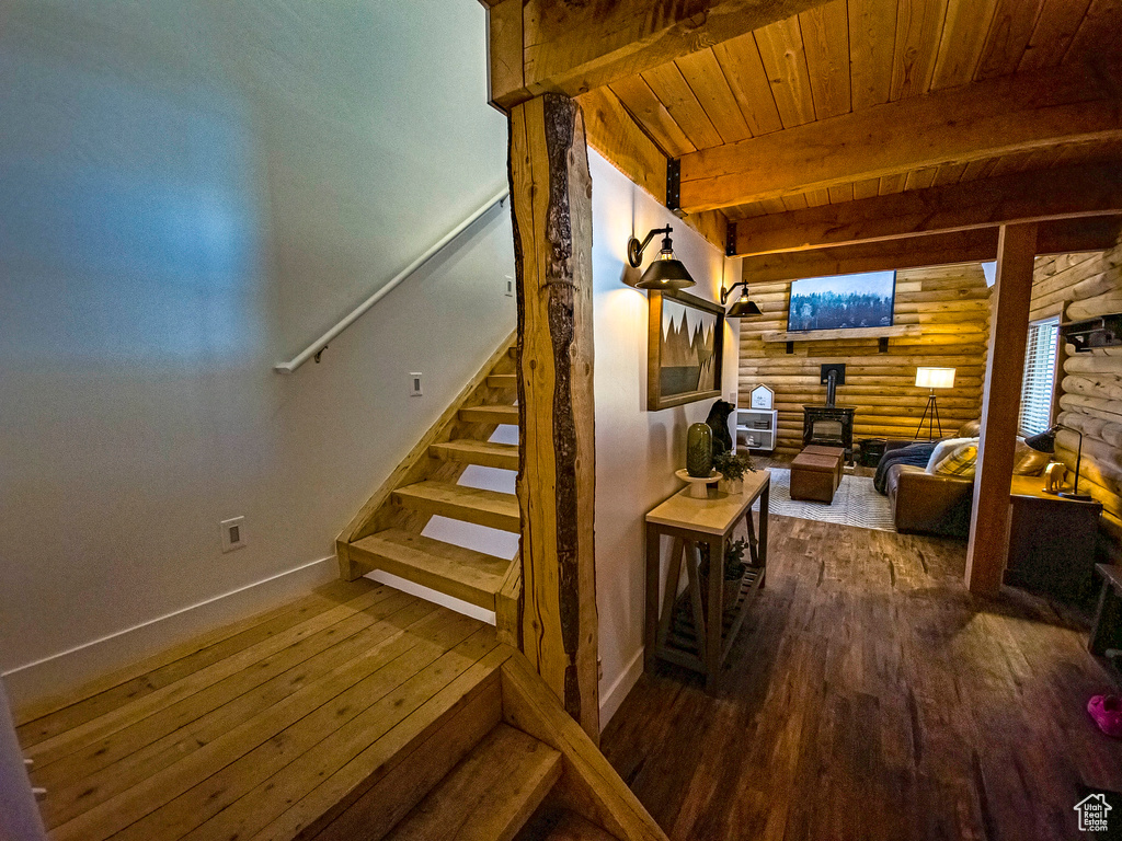 Staircase with dark hardwood / wood-style floors, beam ceiling, a wood stove, wooden ceiling, and log walls