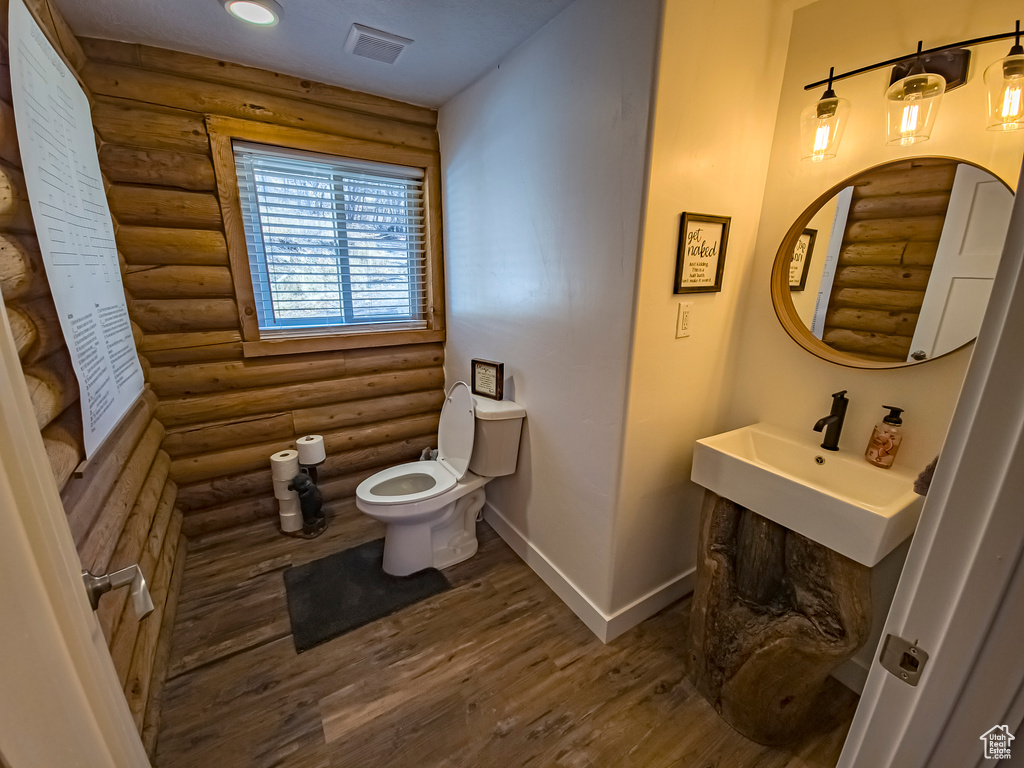 Bathroom with wood-type flooring, vanity, toilet, and rustic walls