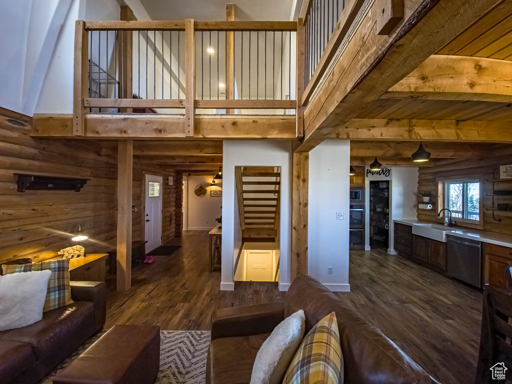 Living room with dark wood-type flooring, rustic walls, sink, and beamed ceiling