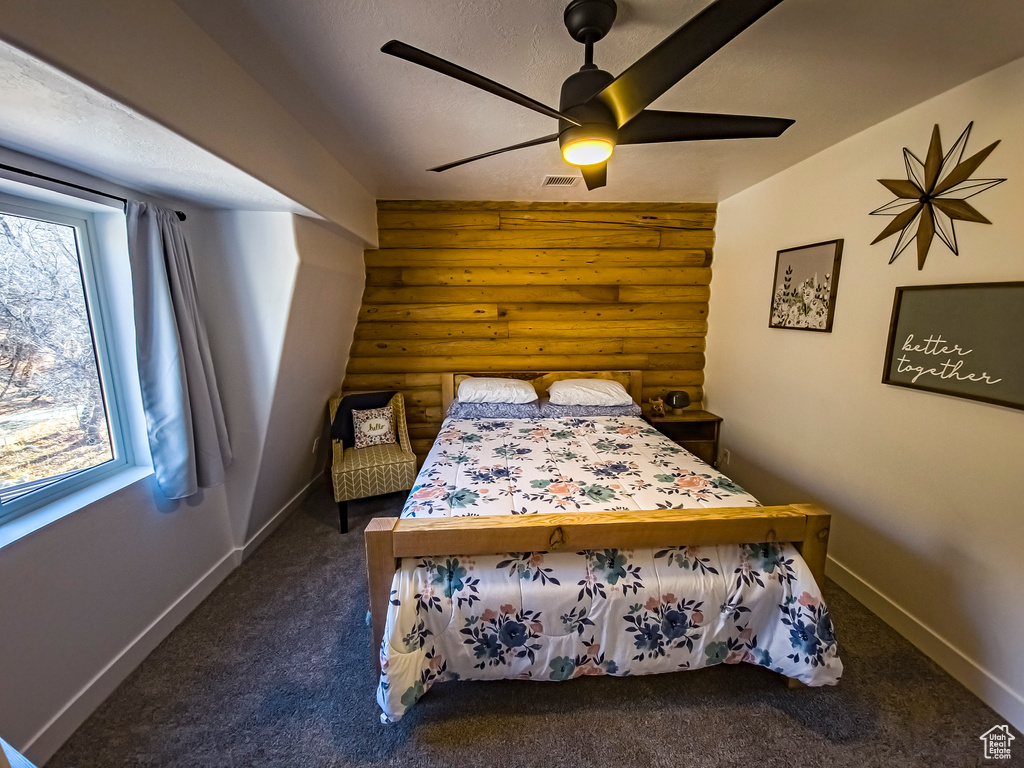 Carpeted bedroom featuring rustic walls and ceiling fan