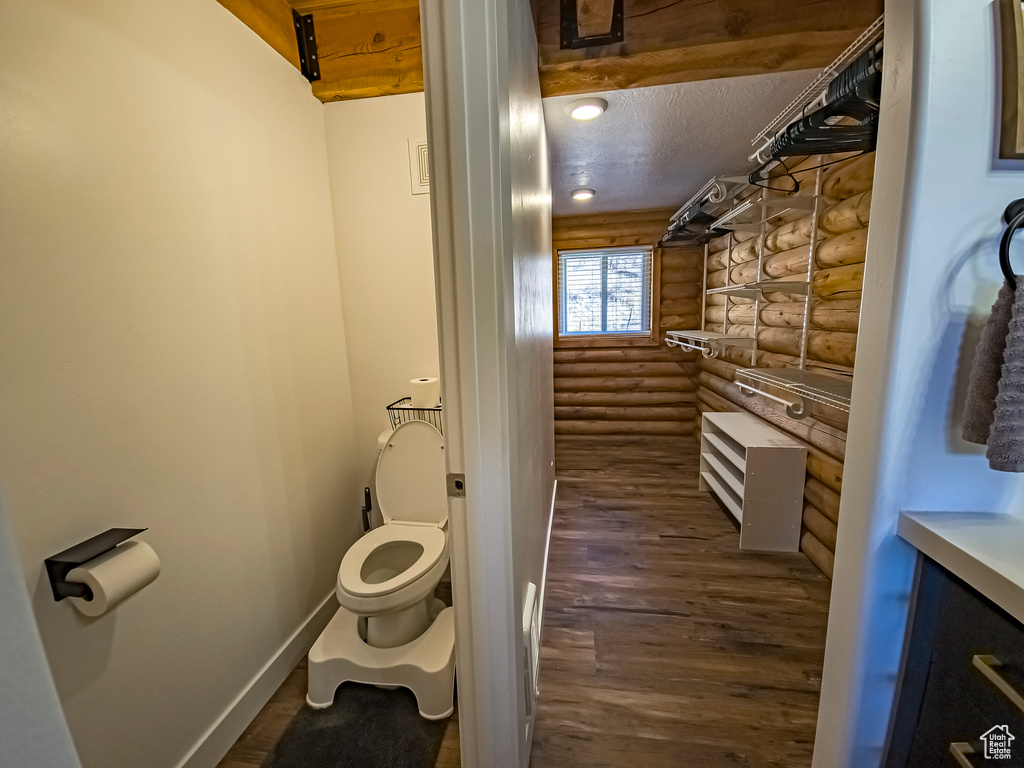 Bathroom featuring a textured ceiling, rustic walls, hardwood / wood-style floors, vanity, and toilet