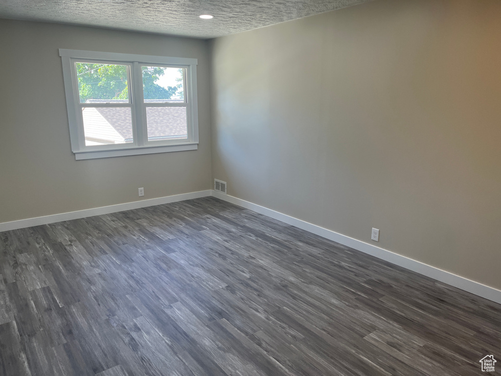 Empty room with dark wood-type flooring and a textured ceiling