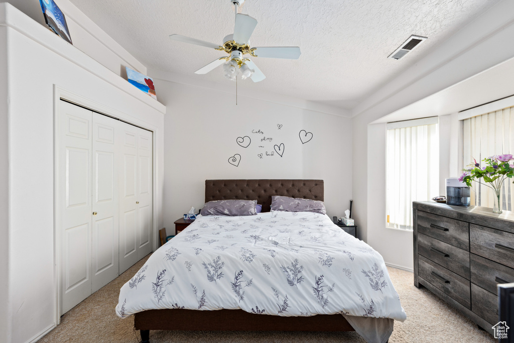 Bedroom with a textured ceiling, a closet, light colored carpet, and ceiling fan