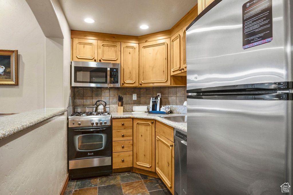 Kitchen featuring backsplash, stainless steel appliances, dark tile floors, light stone counters, and sink