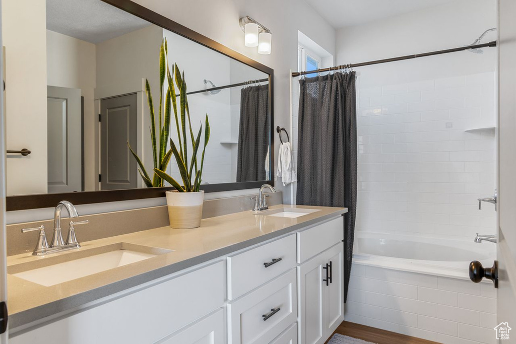 Bathroom featuring dual bowl vanity, shower / tub combo, and hardwood / wood-style floors