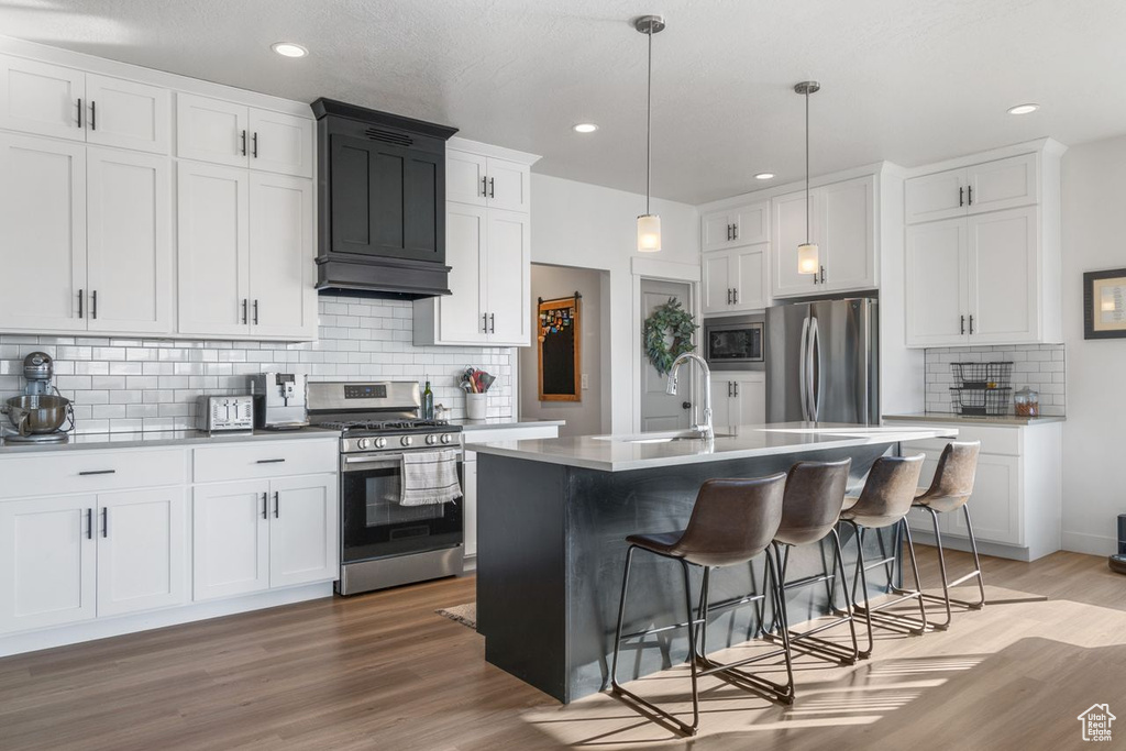 Kitchen with pendant lighting, stainless steel appliances, light hardwood / wood-style floors, and tasteful backsplash