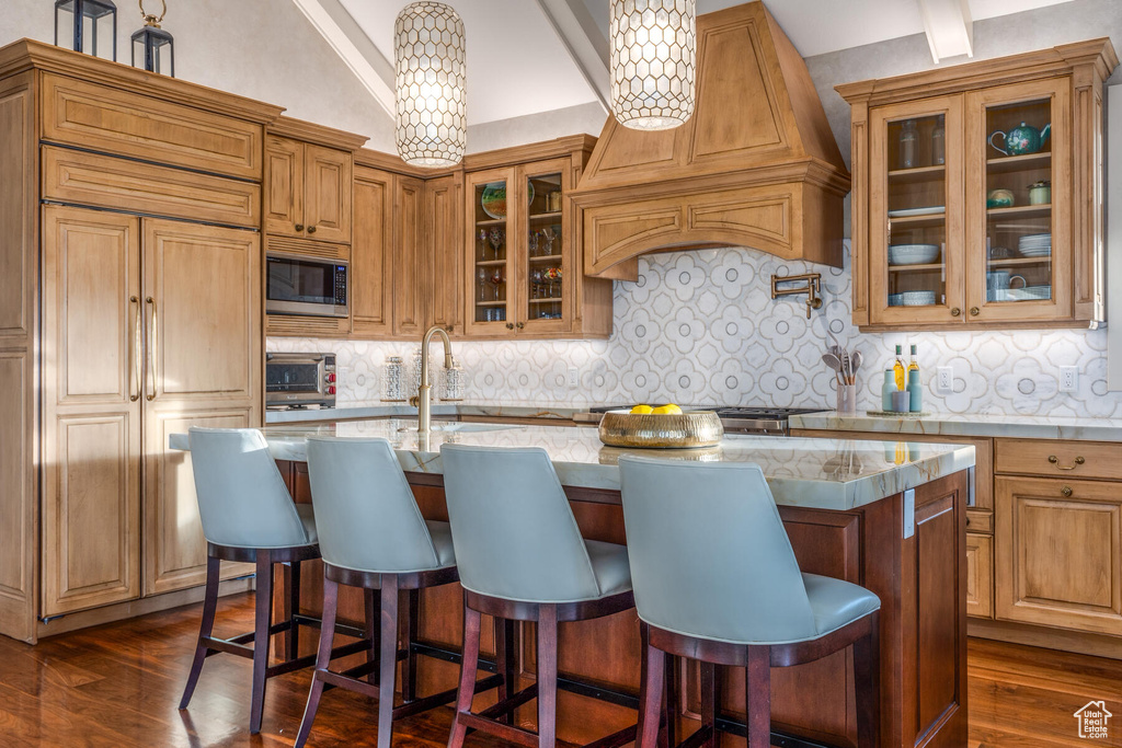 Kitchen with a kitchen island with sink, built in appliances, pendant lighting, and backsplash