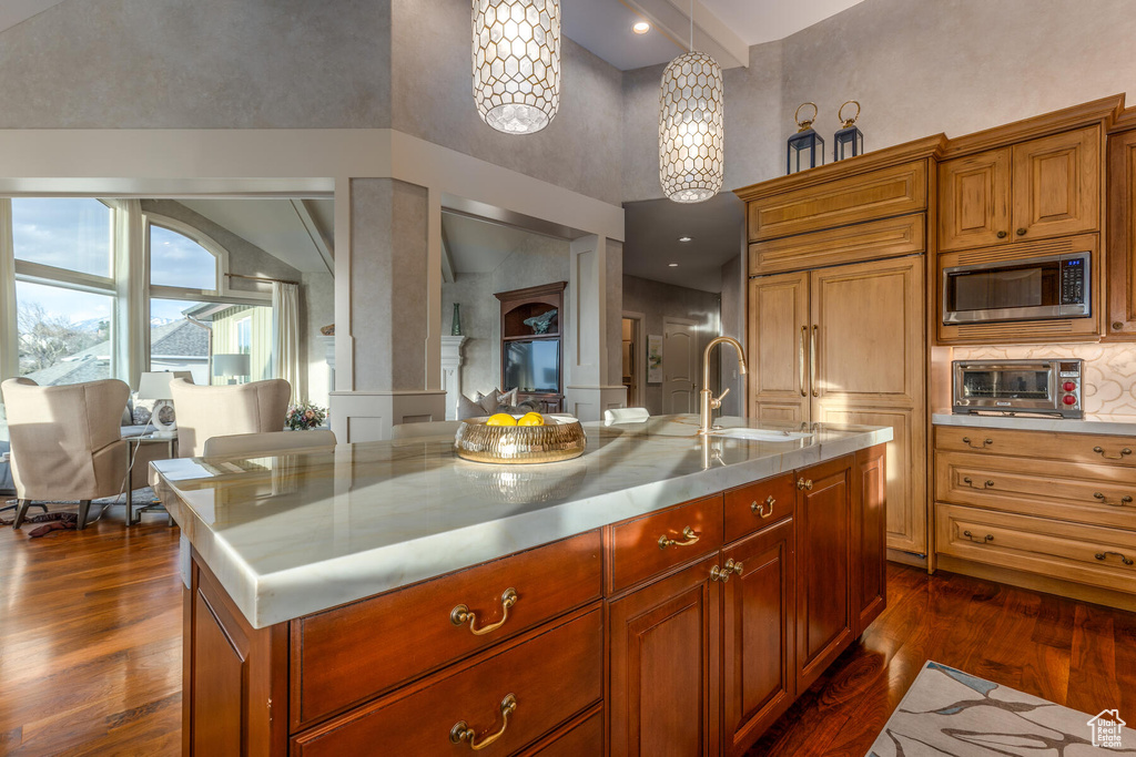 Kitchen with dark hardwood / wood-style floors, an island with sink, stainless steel counters, stainless steel microwave, and sink