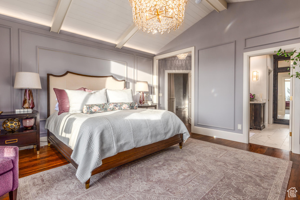 Bedroom with lofted ceiling with beams, an inviting chandelier, connected bathroom, and wood-type flooring