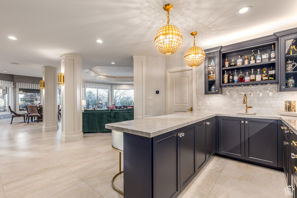 Kitchen with a tray ceiling, kitchen peninsula, tasteful backsplash, pendant lighting, and light tile floors