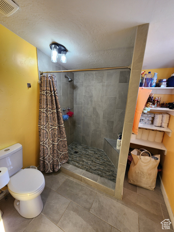 Bathroom with a textured ceiling, toilet, a shower with shower curtain, and tile floors