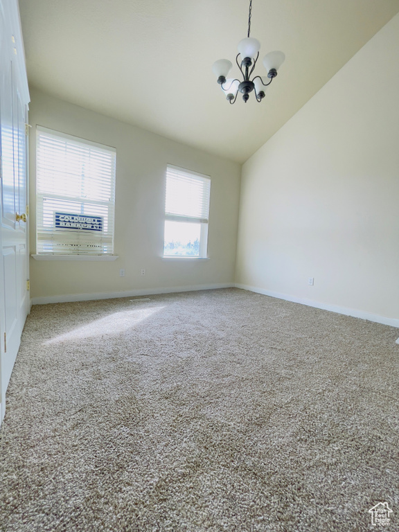 Carpeted spare room featuring lofted ceiling and a notable chandelier