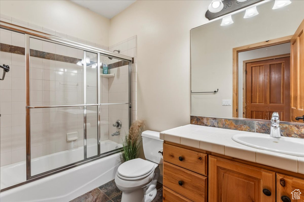 Full bathroom with toilet, oversized vanity, tile floors, and shower / bath combination with glass door