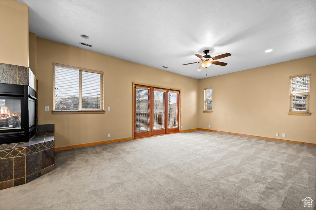 Unfurnished living room with light colored carpet, ceiling fan, and a tile fireplace