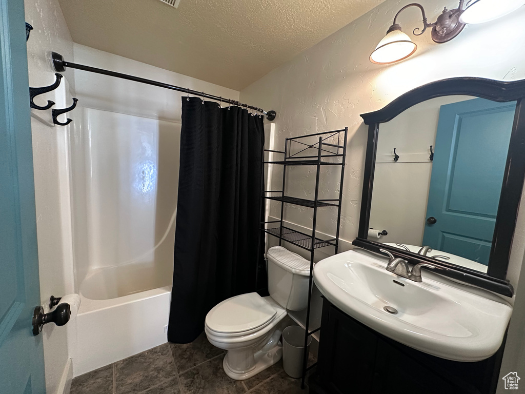 Full bathroom featuring a textured ceiling, tile floors, vanity, shower / bath combo, and toilet