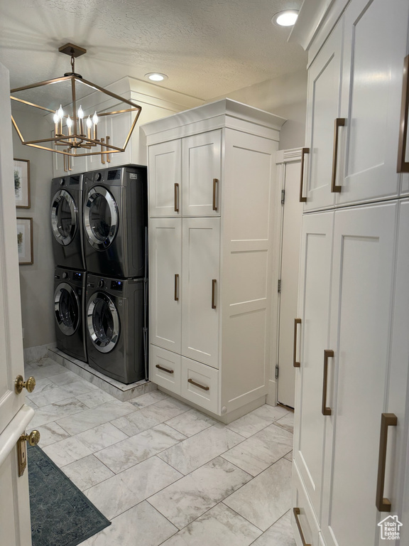 Washroom with a textured ceiling, a chandelier, stacked washer and clothes dryer, and light tile floors