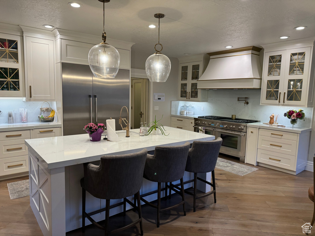 Kitchen featuring custom range hood, white cabinetry, hardwood / wood-style floors, and high end appliances