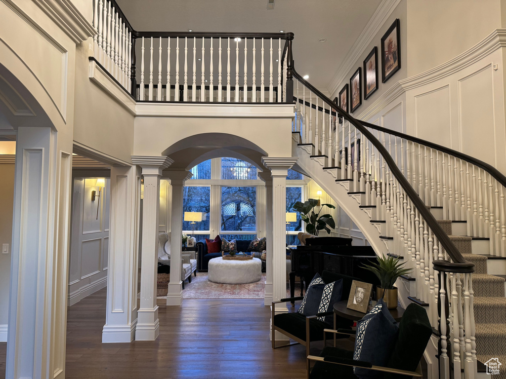 Entryway with dark wood-type flooring, ornamental molding, a towering ceiling, and decorative columns