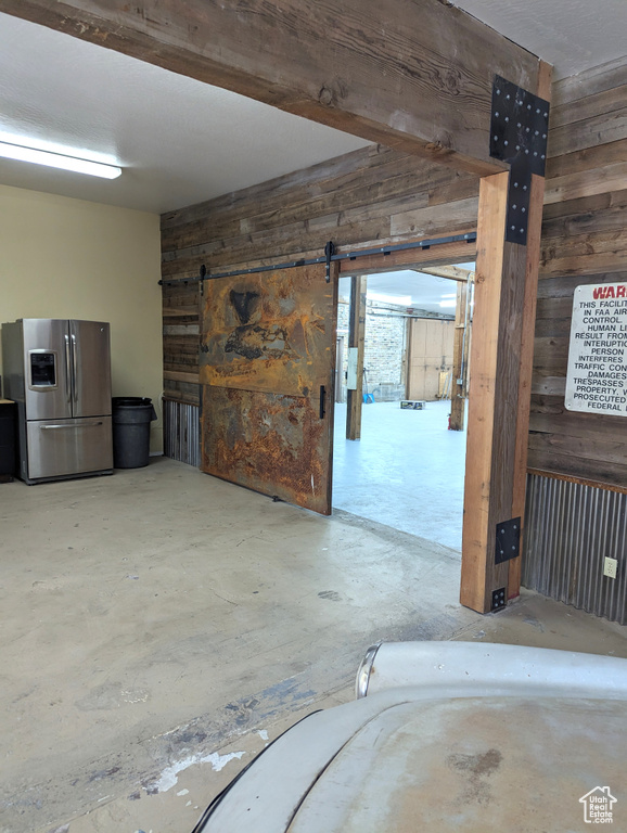 Basement featuring wooden walls, a barn door, and stainless steel fridge with ice dispenser