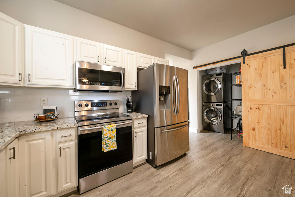 Kitchen featuring stacked washer / drying machine, light hardwood / wood-style floors, a barn door, stainless steel appliances, and light stone countertops