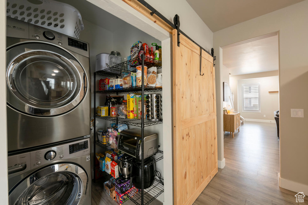 Laundry room with stacked washer / drying machine, a barn door, and light wood-type flooring
