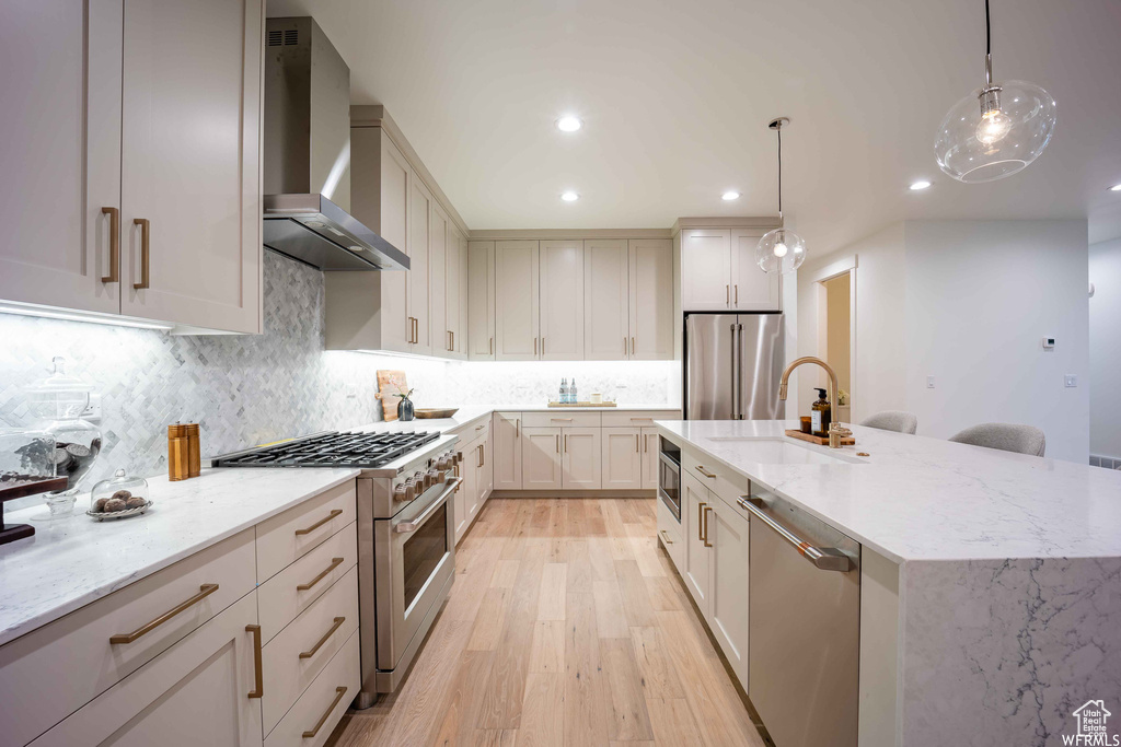 Kitchen with wall chimney range hood, light hardwood / wood-style flooring, premium appliances, and light stone counters