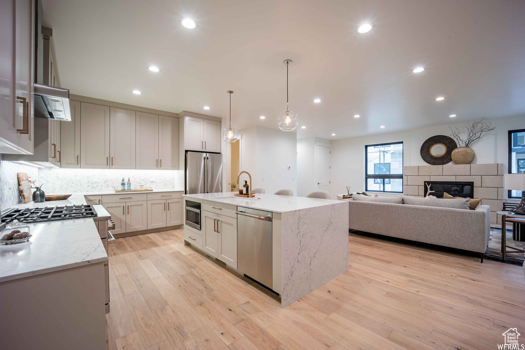 Kitchen featuring light wood-type flooring, a tile fireplace, a kitchen island with sink, and stainless steel appliances