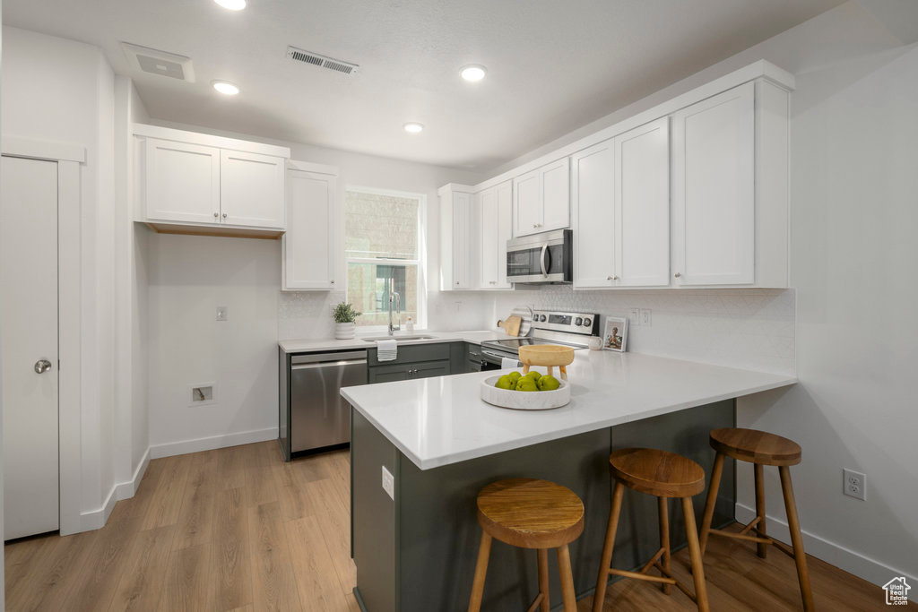 Kitchen with a breakfast bar, light hardwood / wood-style floors, backsplash, stainless steel appliances, and kitchen peninsula