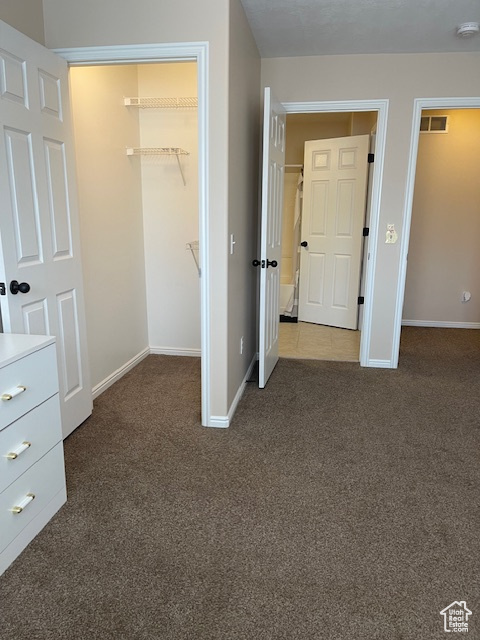 Unfurnished bedroom featuring a closet, a spacious closet, and dark carpet