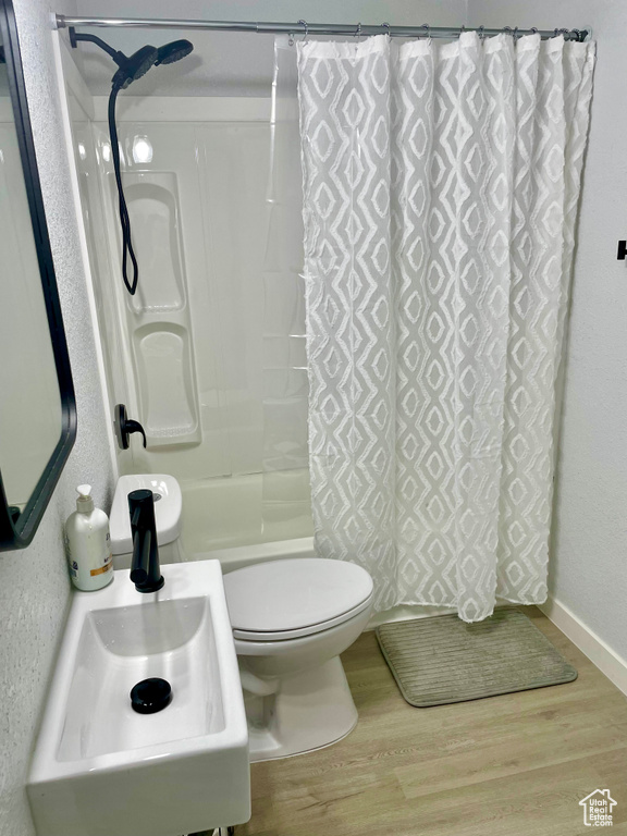 Full bathroom featuring shower / bath combo with shower curtain, sink, hardwood / wood-style floors, and toilet