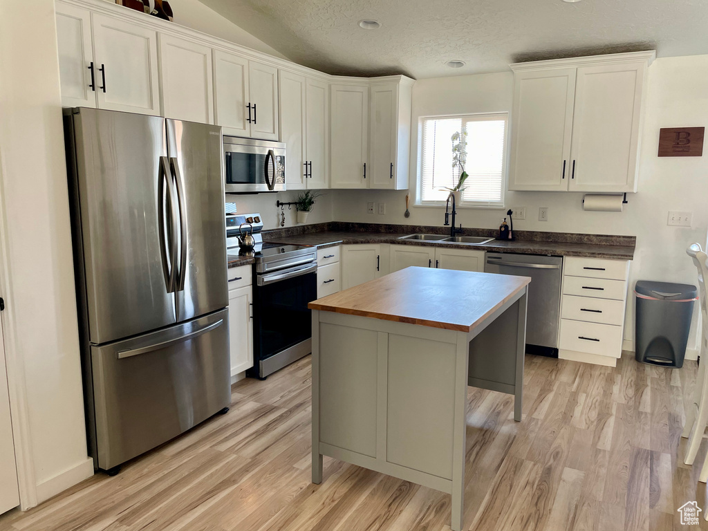 Kitchen featuring appliances with stainless steel finishes, light hardwood / wood-style floors, white cabinetry, sink, and a kitchen island