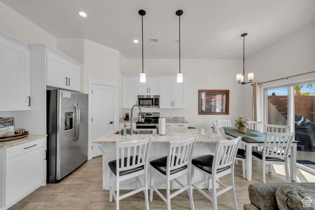 Kitchen featuring a kitchen island with sink, white cabinetry, pendant lighting, an inviting chandelier, and appliances with stainless steel finishes