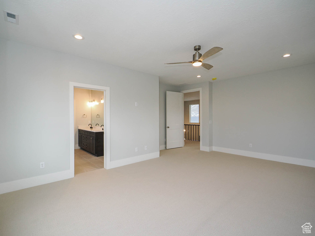 Unfurnished bedroom with light colored carpet, ensuite bathroom, sink, and ceiling fan