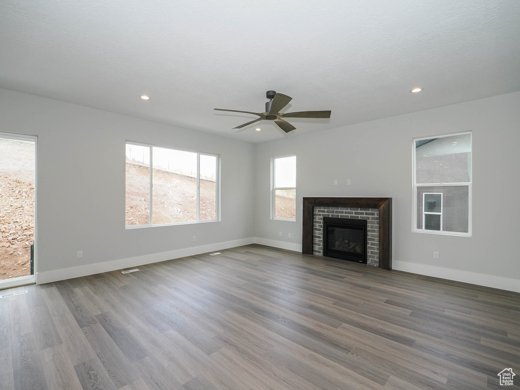 Unfurnished living room with a brick fireplace, dark wood-type flooring, and ceiling fan