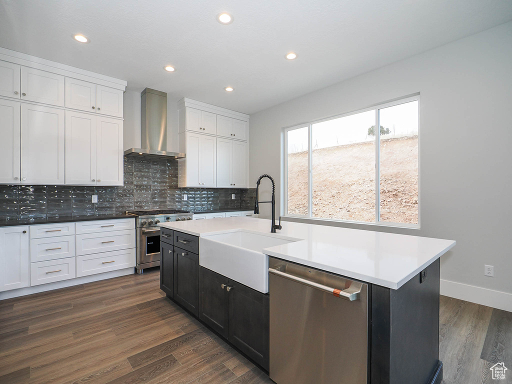 Kitchen featuring sink, an island with sink, dark hardwood / wood-style floors, appliances with stainless steel finishes, and wall chimney range hood