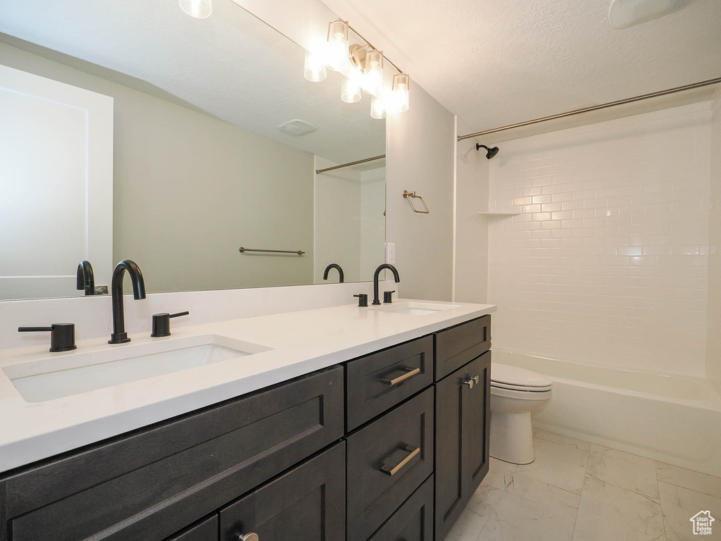Full bathroom with a textured ceiling, tiled shower / bath, dual bowl vanity, toilet, and tile flooring