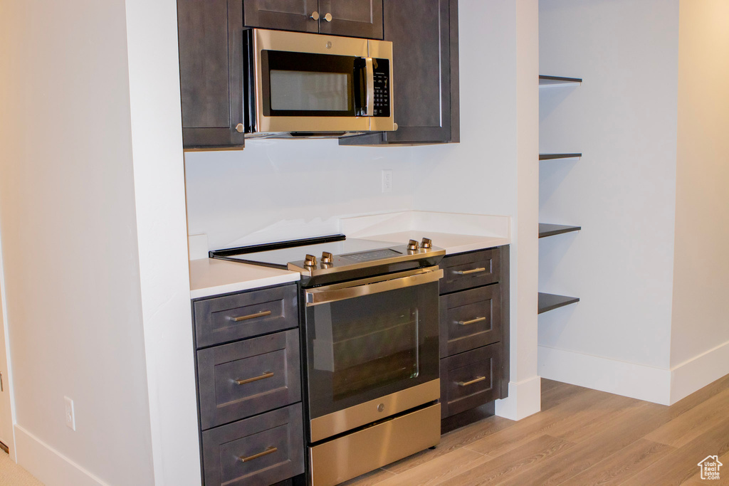 Kitchen with appliances with stainless steel finishes, dark brown cabinets, and light hardwood / wood-style flooring